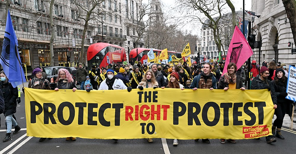 Eight protestors hold a long yellow Extinction Rebellion banner which reads 'Protect The Right To Protest' as they lead a protest march along a central London street.  