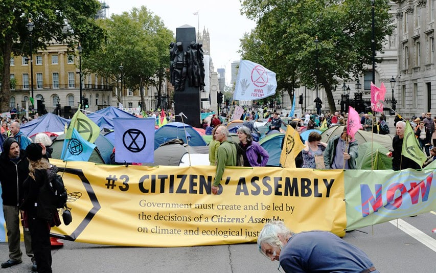 Demonstranten halten ein XR Schild hoch mit der Aufschrift "#3 Citizens'Assembly"treet 