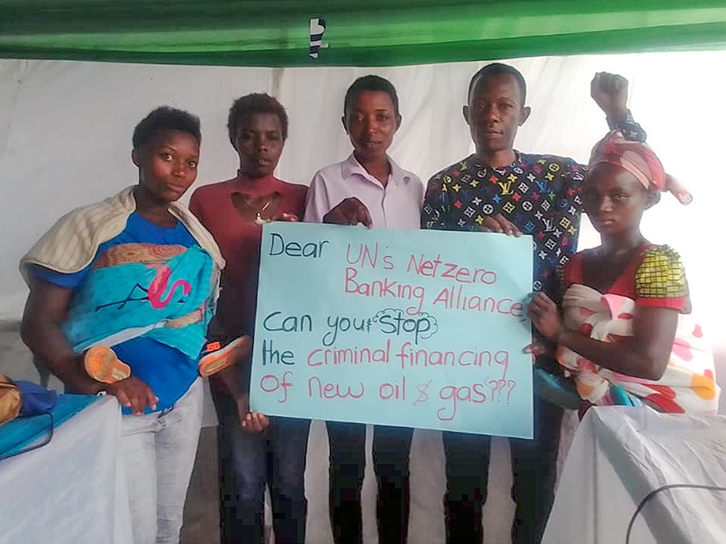 L'autore David Jesero è in piedi con quattro donne che reggono un cartellocon la scritta: Cara Alleanza Bancaria Net-Zero dell'ONU, puoi fermare ilfinanziamento criminale di nuovo petrolio egas??