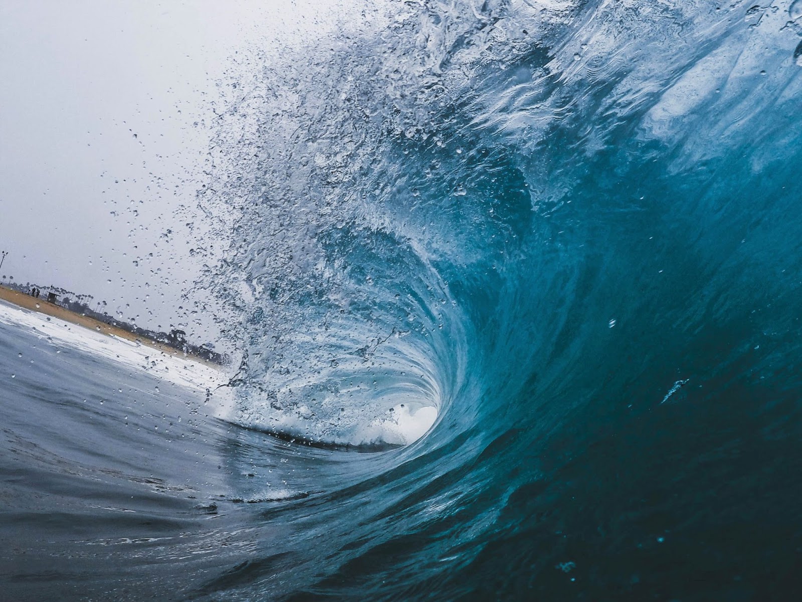 The barrel of a crystal blue wave crashing down towards the shore, with the crest spraying water.