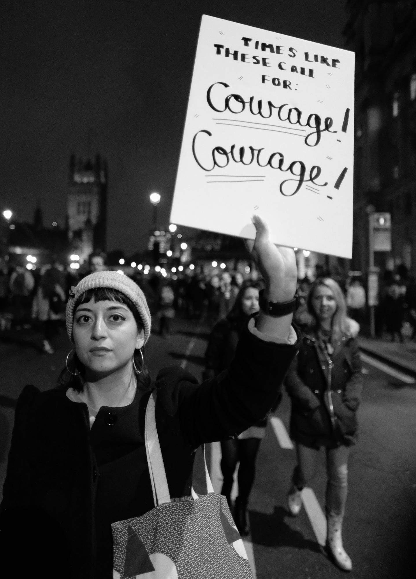 A woman in a march holds a sign saying "Times like these call for courage! Courage!"
