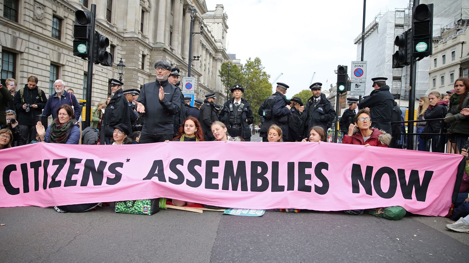 Imagem de manifestantes bloqueando uma rua com uma grande faixa com aspalavras "assembleias de cidadãosagora".