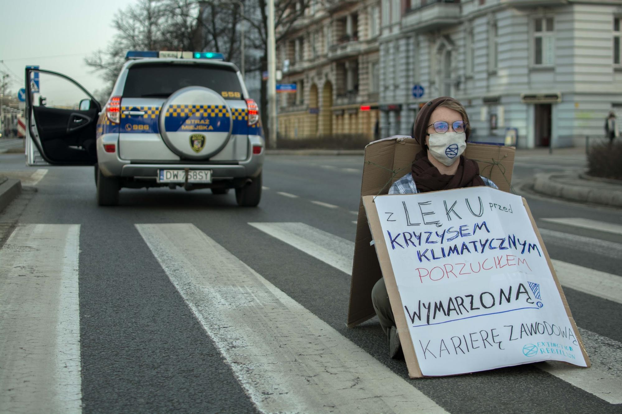 A Rebellion of One in Wrocław. Lone rebels (with hidden support teams)blocked roads across Poland. The banner: ‘Climate crisis fears made me dropmy dream career’. Photo: cyjon & AlicjaKozuchowska
