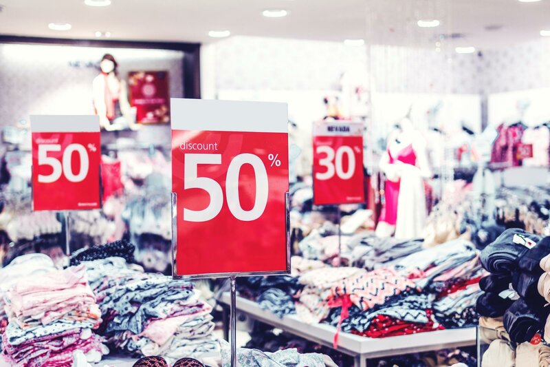 Bild mit 50%-Rabatt-Schildern in einem Fast-Fashion-Outlet mit haufenweiseKleidung auf den Tischen drum herum
