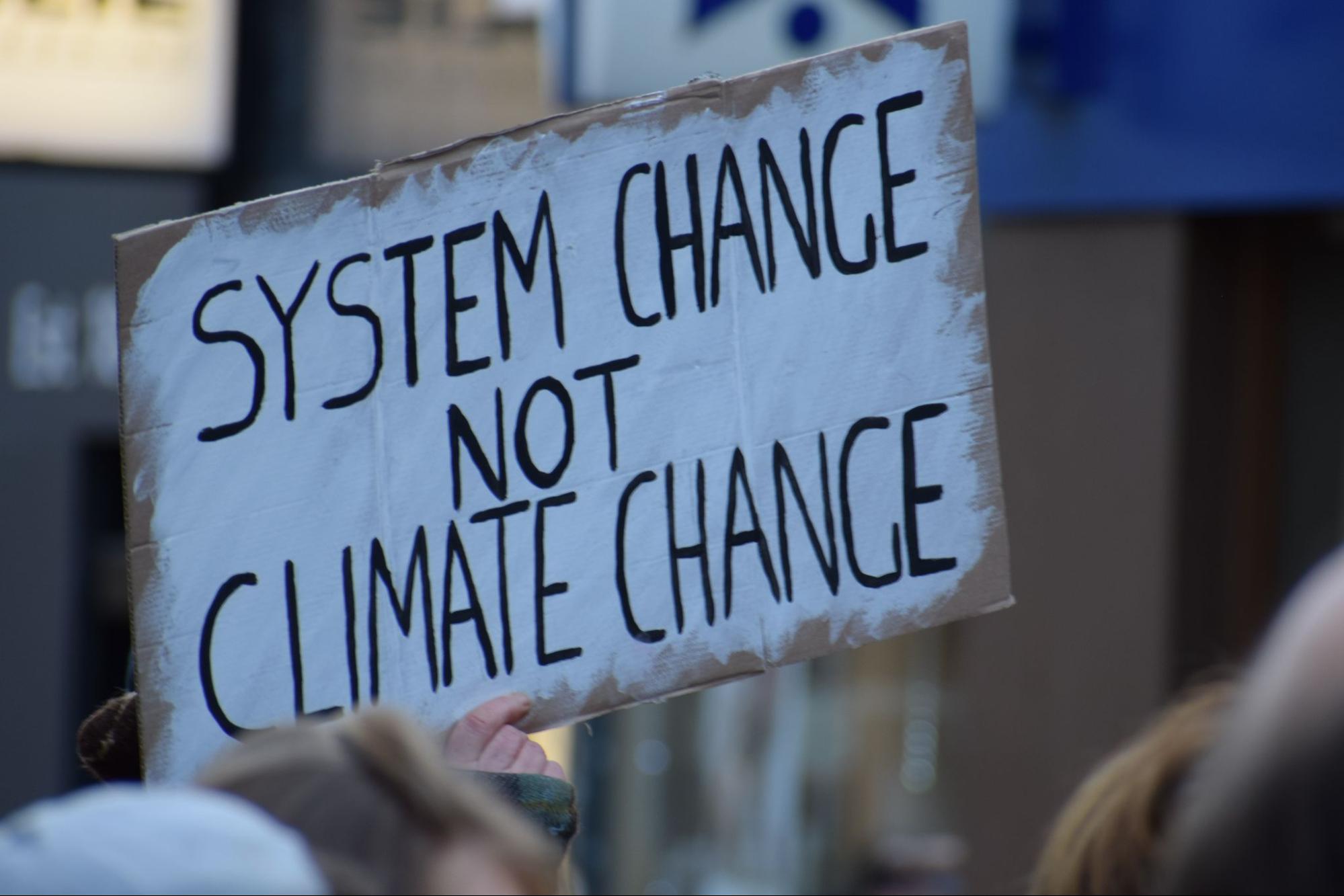 Cardboard sign held aloft with painted words stating: "System change not climate change"
