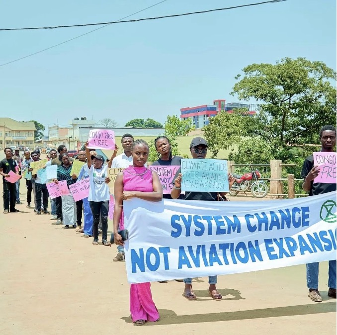 A photo of a group of people standing in a line holding protest signs and banners with messages such as "system change not aviation expansion".