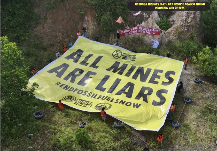 Photo of a large yellow banner held by protesters in a forested area, with text "ALL MINES ARE LIARS #ENDFOSSILFUELSNOW".