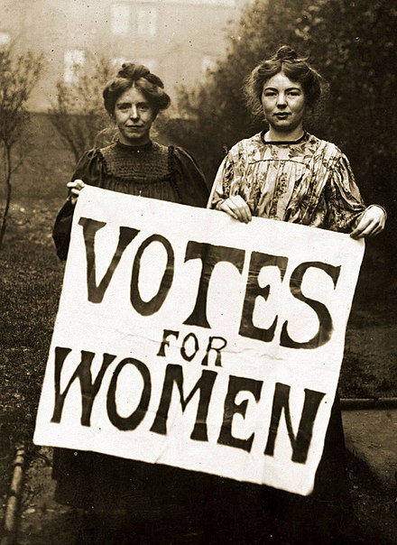 Historic image of two women holding up a sign with the words "Votes for Women" on it.