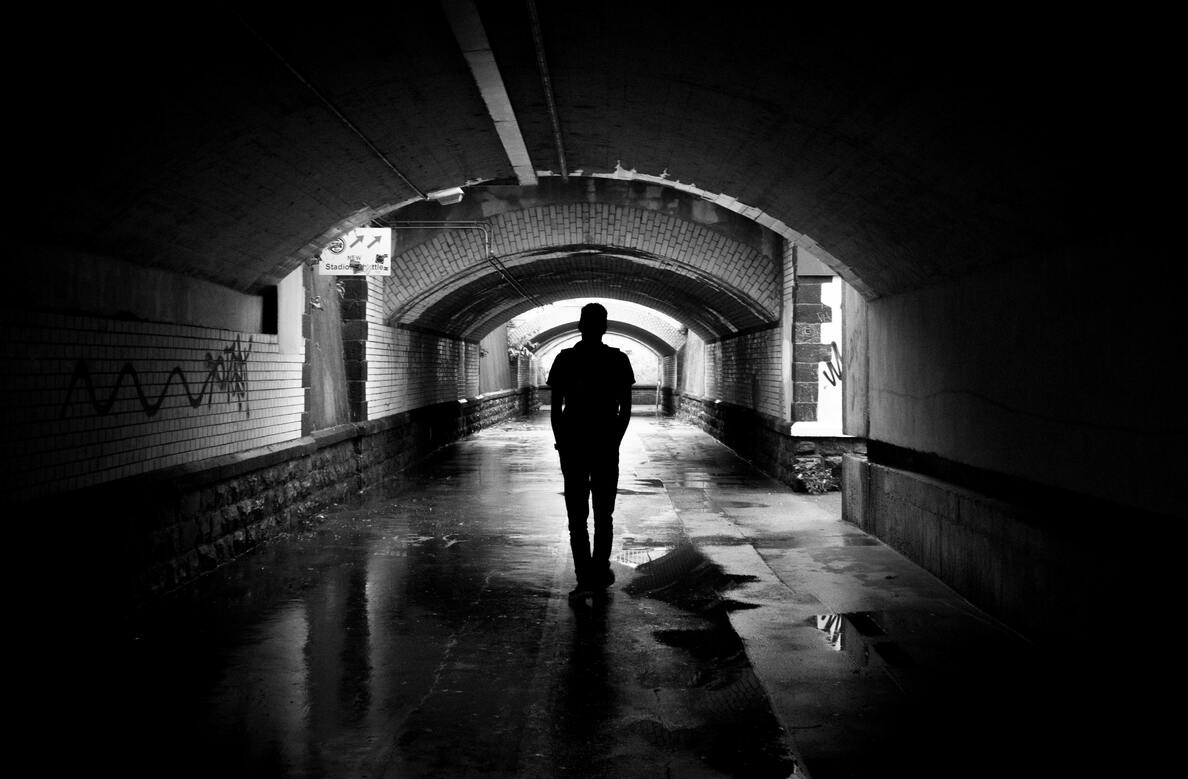 A black and white photo showing a person silhouetted in a dark tunnel