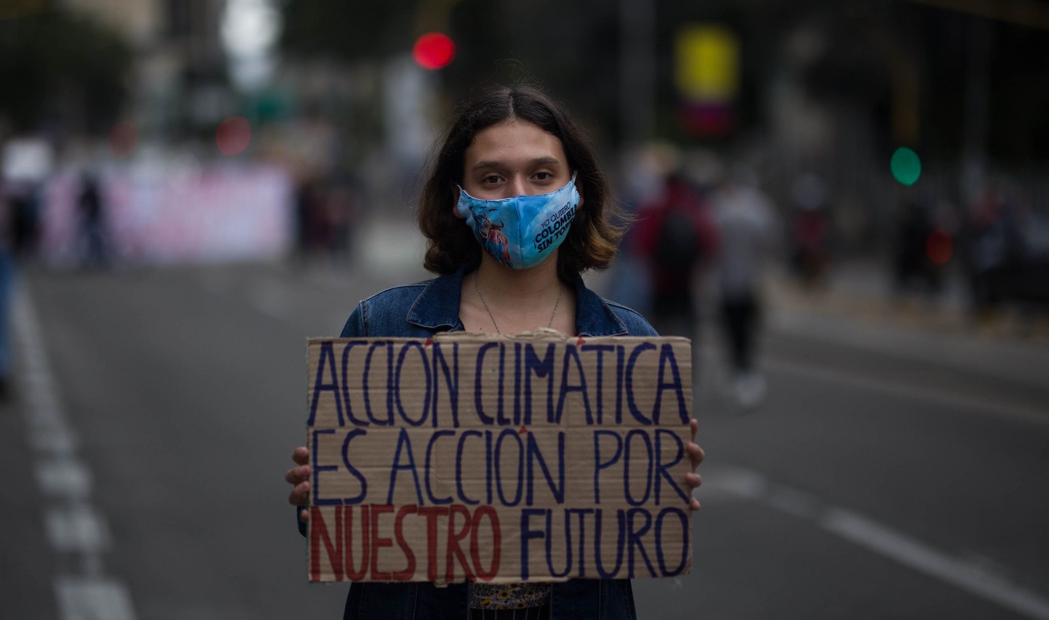 A young woman wearing a face mask holds a sign while stood in the road