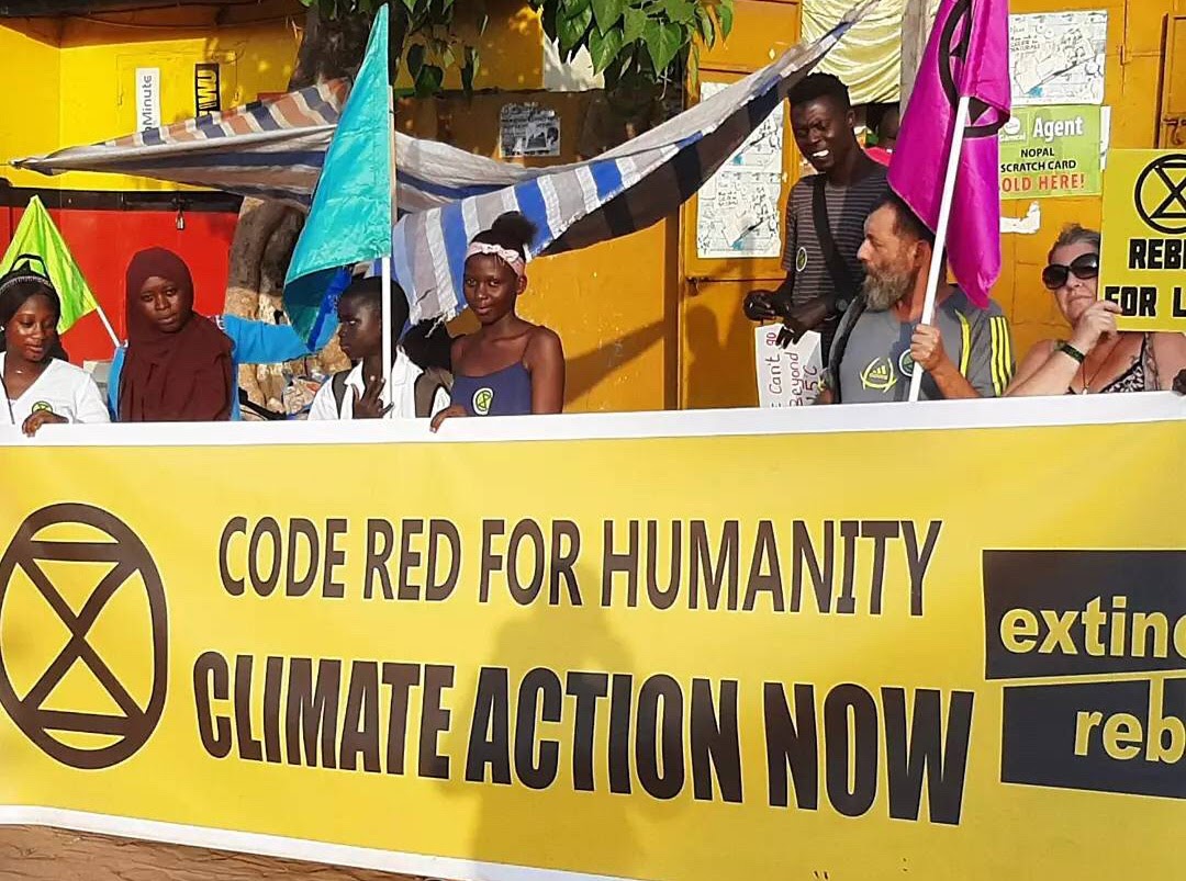Rebels stand behind a long yellow Extinction Rebellion banner which reads 'Code Red For Humanity - Climate  Action Now.'