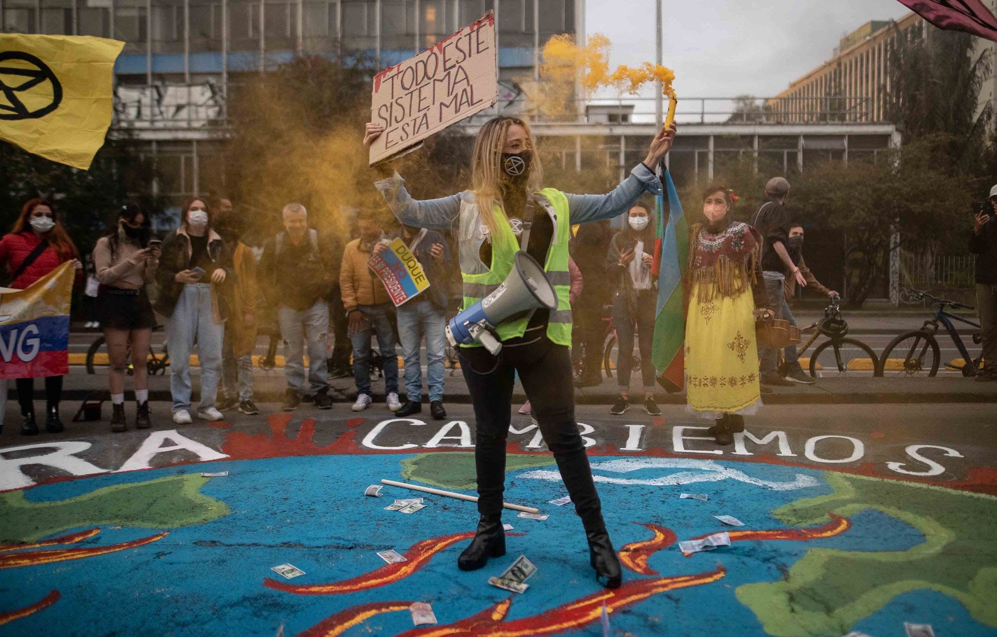 A young woman stands in the centre of an earth mural holding a yellow flare and sign.