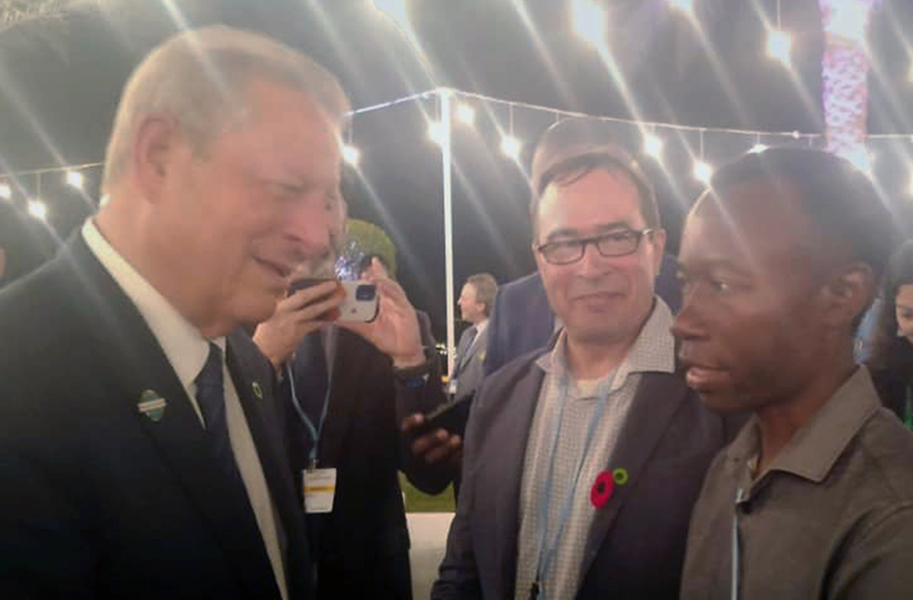 Nesta foto nocturna no exterior com luzes suspensas, o ex-vice-presidentedos EUA, Al Gore e autor deste artigo, David Jesero, estão a sorrir. Umhomem não identificado, também sorrindo, está entreeles.)