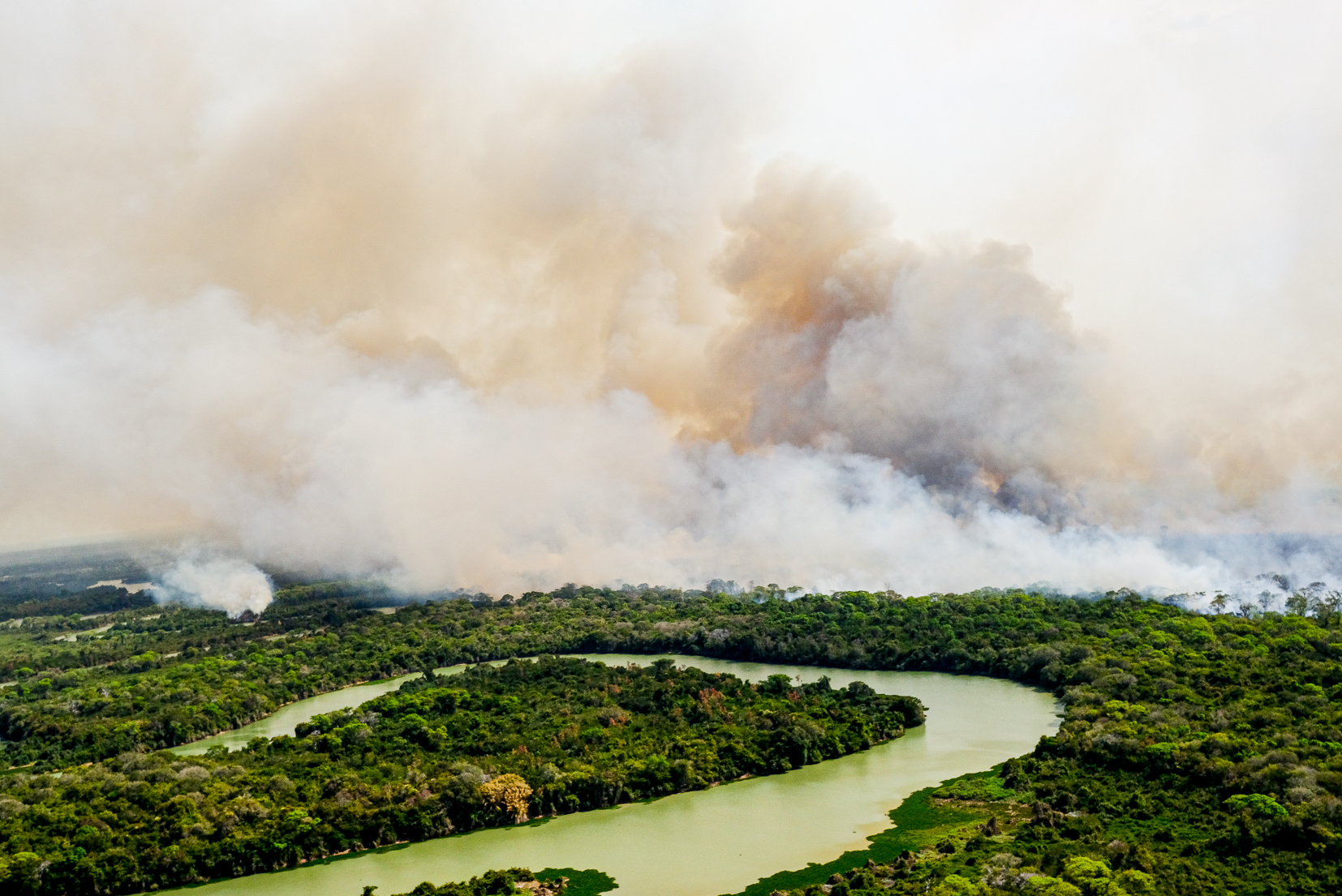 A section of rainforest is shown from above, with the river bending back on itself, and a great plume of smoke enveloping the forest in the background.