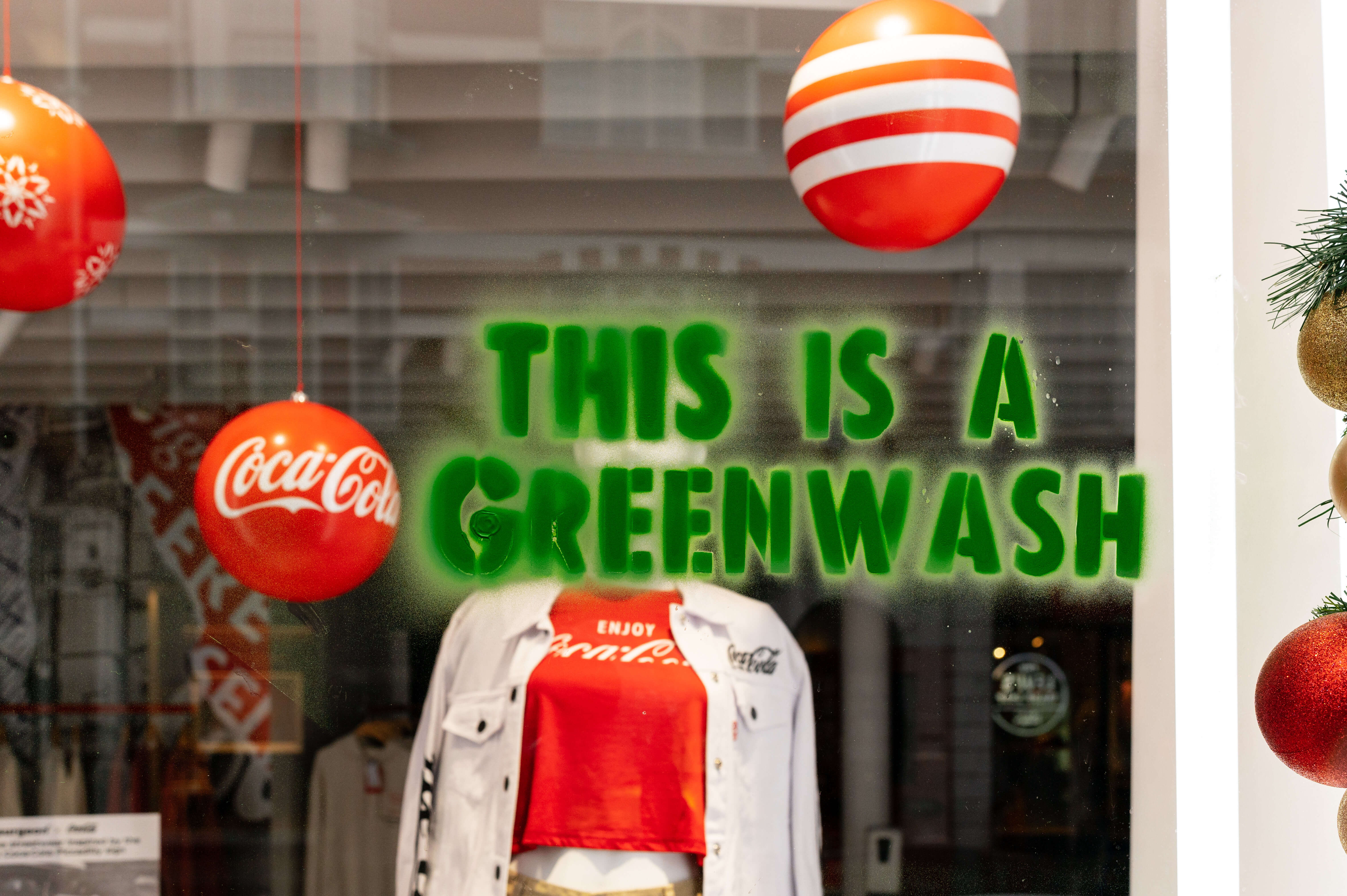 Image shows "This is Greenwash" stencilled onto the front of a Coca-Cola shop in London