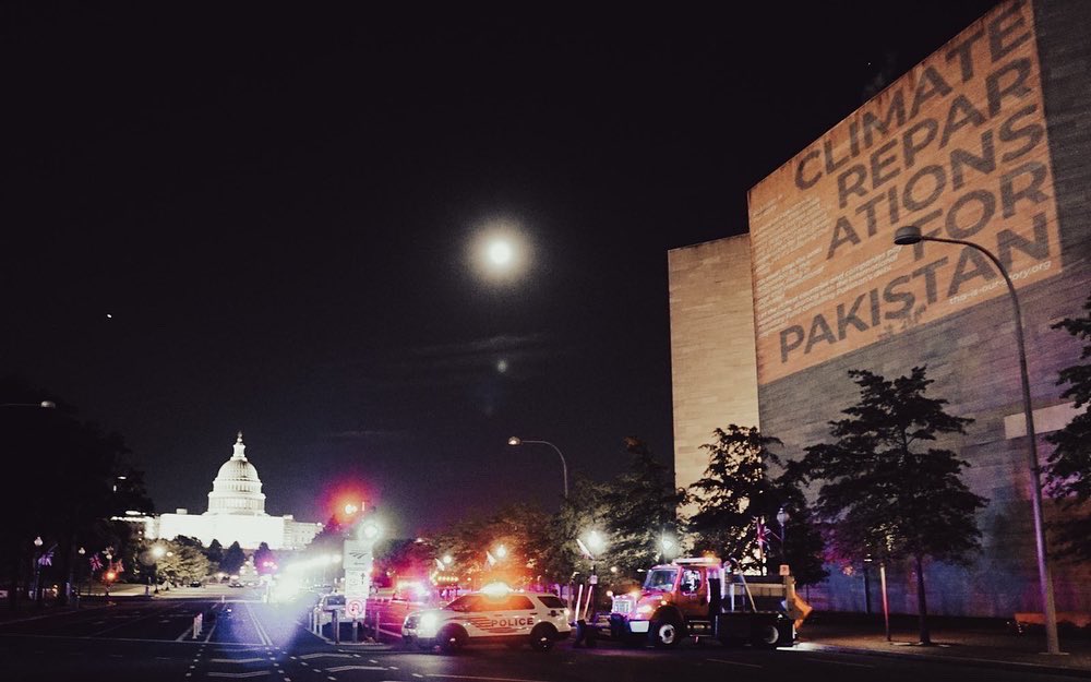 "Climate Reparations for Pakistan" projected onto the side of the US Capitol building at night, with the White House in the back left.