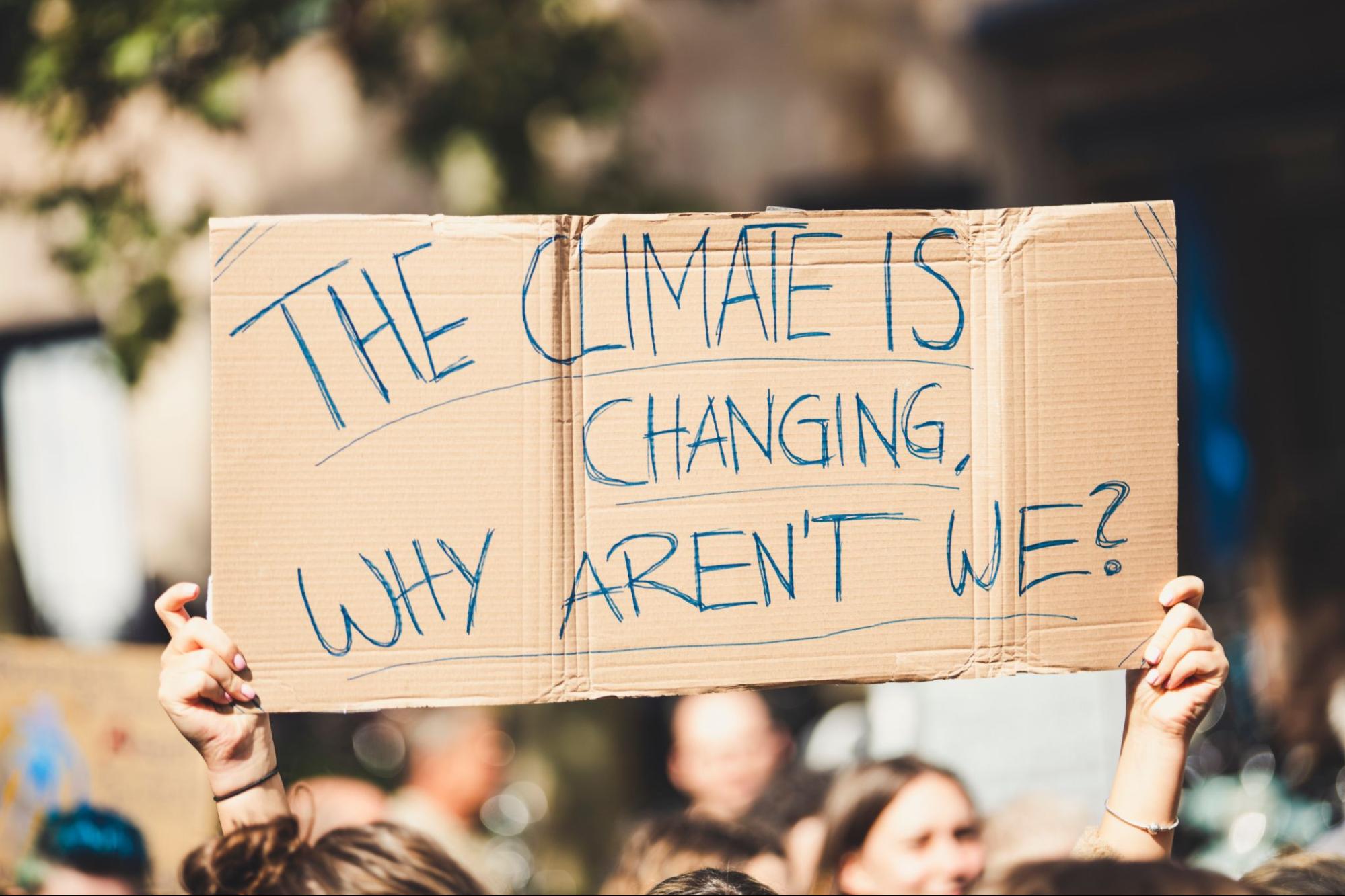 Des bras brandissant une pancarte disant : "Le climat change, pourquoi nele faisons-nous pas ?" lors d'une manifestation pour leclimat