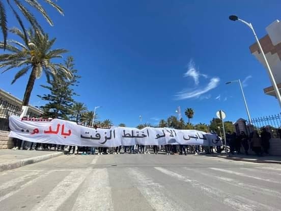 Image of protesters in Gabès holding a sign roughly translating to ‘Gabès in Pain, Asphalt mixed with Blood’